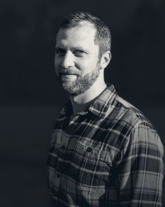 Tim Speciale in black and white, in a plaid shirt against a dark background